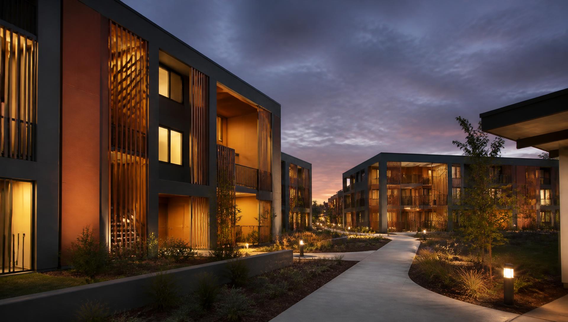 Dusk view of a modern employee housing community with warm lit windows and landscaped walkways